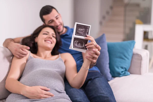 Mladí Těhotná Pár Hledá Ultrazvuk Foto Dítěte Při Odpočinku Pohovce — Stock fotografie