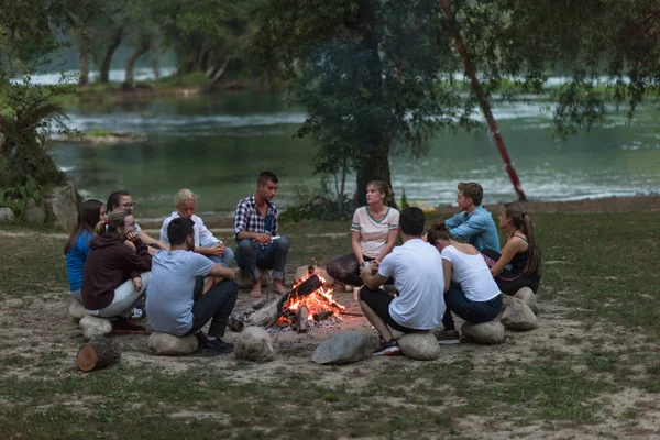 친구들이 강둑에서 모닥불 주위에서 저녁을 즐기면서 휴식을 취하고 — 스톡 사진