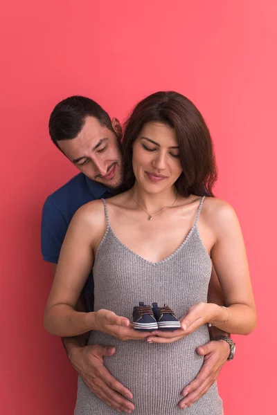 Jong Zwanger Koppel Houden Pasgeboren Baby Schoenen Geïsoleerd Rode Achtergrond — Stockfoto