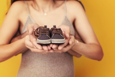 Yeni doğan bebek patiği izole sarı arka plan, Aile ve ebeveynlik kavramı üzerinde tutan genç hamile Çift