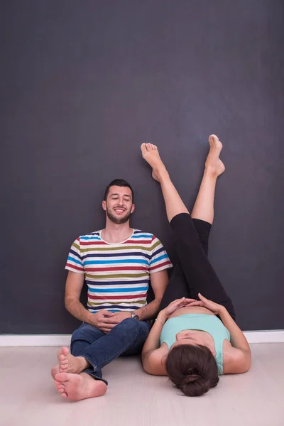 幸福的怀孕夫妇在家里地板上的黑色黑板前放松 — 图库照片