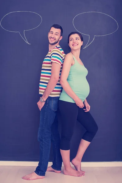 年轻的怀孕夫妇想到他们未出生的婴儿的名字 并写在一个黑色的黑板上 — 图库照片