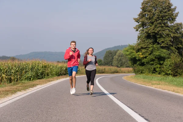 田舎道をジョギングしながら健康な生活を楽しんでいる若いカップル運動とフィットネスの概念 — ストック写真