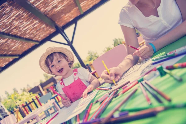 年轻的母亲和她的小女儿愉快地在一起 一边用铅笔蜡笔 一边在外面的游戏学校画一幅五颜六色的画 — 图库照片