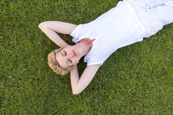 年轻女子在草地上放松 同时双手背在脑后 放松和自然概念的最高视野 — 图库照片