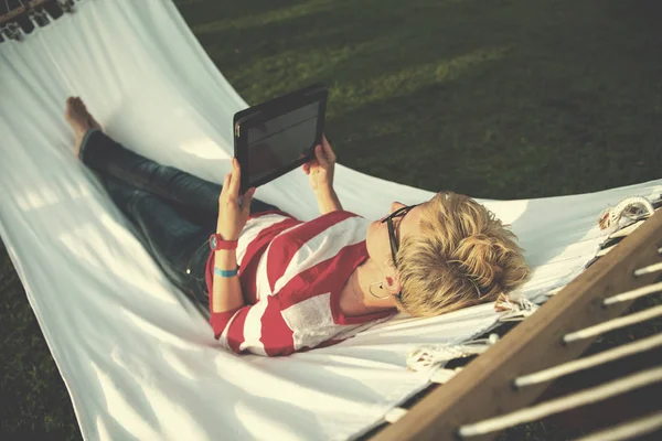 年轻女子在度假时在宁静的花园里的吊床上放松时 使用平板电脑 — 图库照片