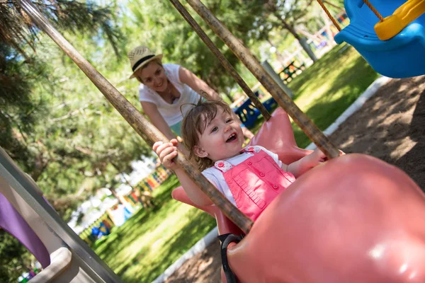 若い母親と公園の遊び場で振り回しながら一緒に笑みを浮かべて彼女の小さな娘 — ストック写真