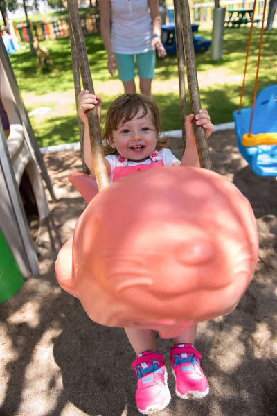 若い母親と公園の遊び場で振り回しながら一緒に笑みを浮かべて彼女の小さな娘 — ストック写真
