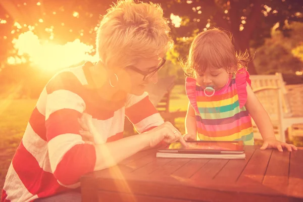 快乐的母亲和她的小女儿享受自由时间使用平板电脑 而在假期花园放松在阳光明媚的日子 — 图库照片