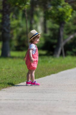 Şapkalı sevimli küçük kız yaz sabahı Park 'ta koşarken neşeyle vakit geçiriyor.