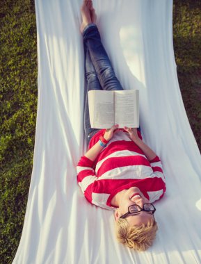 Genç kadın huzurlu bir bahçe hamakta üzerinde rahatlatıcı tatil sırasında bir kitap okuma