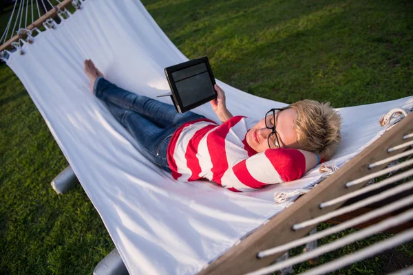 若い女性の休暇中に静かな庭園でハンモックでリラックスしながらタブレット コンピューターを使用して — ストック写真