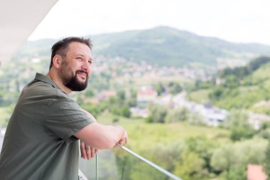 Arka planda şehir manzaralı bir modern balkon ayakta başarılı mutlu genç hipster adam portresi