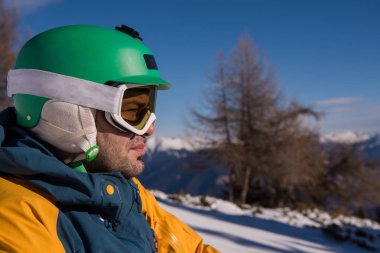 Kış mevsiminde güneşli bir günde dinlenen ve poz veren snowboardcu.