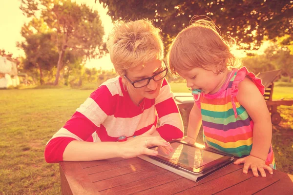 快乐的母亲和她的小女儿享受自由时间使用平板电脑 而在假期花园放松在阳光明媚的日子 — 图库照片