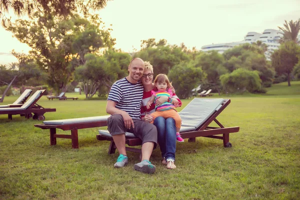年轻幸福家庭的肖像与一个小女儿坐在阳光床上在美丽的热带公园 — 图库照片