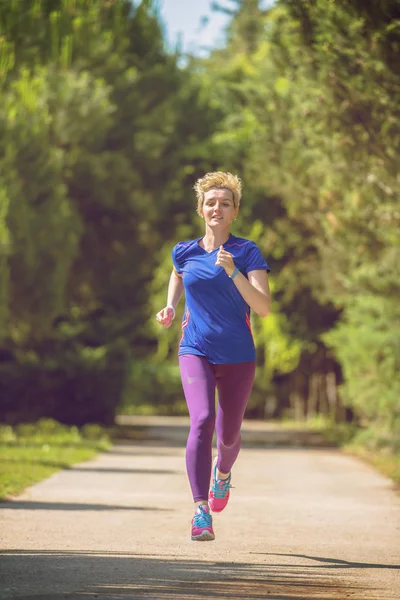 若いスポーティな女性ランナーの晴れた朝の美しい熱帯公園でマラソンのトレーニング — ストック写真