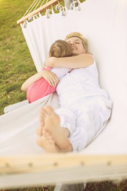 Mutlu anne ve küçük bir kızı zevk boş zamanlarımda sarılma ve bir hamakta güneşli bir gün boyunca tatil ev bahçe üzerinde rahatlatıcı.
