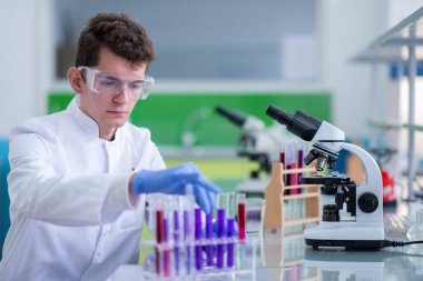 Koruyucu gözlüklü genç öğrenci parlak laboratuvar, eğitim ve tıp konseptinde kimya deneyi yapıyor.