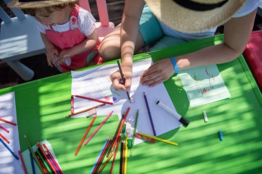 Genç Anne ve onun küçük kızı neşeyle harcama zaman içinde dış anaokulu renkli resimler çizerken kalem boya kalemleri kullanarak birlikte