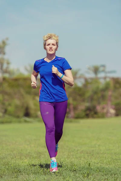 若いスポーティな女性ランナーの晴れた朝の美しい熱帯公園でマラソンのトレーニング — ストック写真