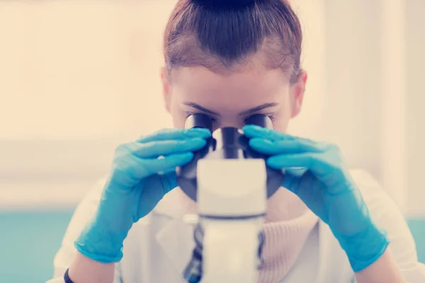 年轻的女学生科学家在实验室做一些研究时通过显微镜观察 — 图库照片