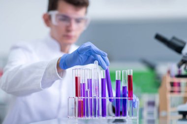 Koruyucu gözlüklü genç öğrenci parlak laboratuvar, eğitim ve tıp konseptinde kimya deneyi yapıyor.