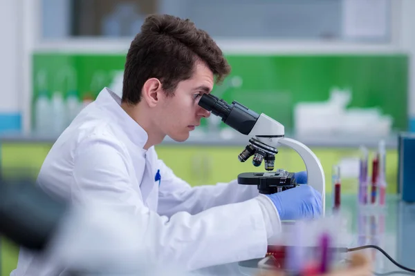年轻的学生科学家在实验室里做一些研究时 通过显微镜观察 — 图库照片
