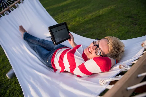 若い女性の休暇中に静かな庭園でハンモックでリラックスしながらタブレット コンピューターを使用して — ストック写真
