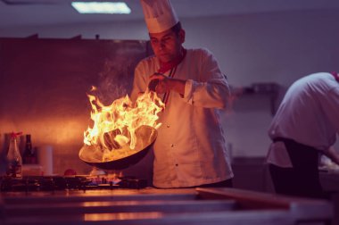 Aşçı lokanta mutfağında yemek pişiriyor ve ateş yakıyor.