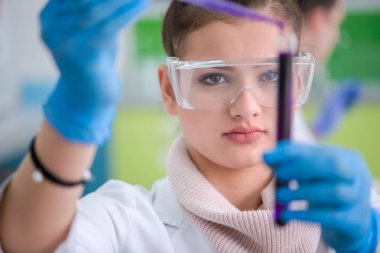 Koruyucu gözlüklü genç kız öğrenci parlak laboratuvar, eğitim ve tıp konseptinde kimya deneyi yapıyor.