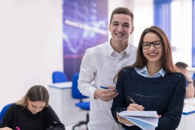 Sınıfta bir proje üzerinde çalışan iki genç kız ve erkek öğrenci notlar yazıp tartışıyorlar.