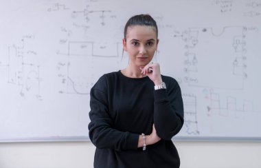 Beyaz karatahtanın önünde duran ve kameraya bakan güzel bir kız öğrencinin portresi.