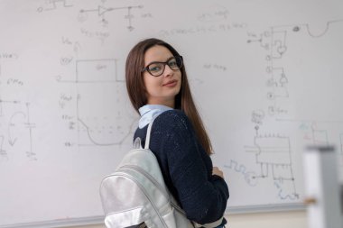 Beyaz karatahtanın önünde duran ve kameraya bakan güzel bir kız öğrencinin portresi.