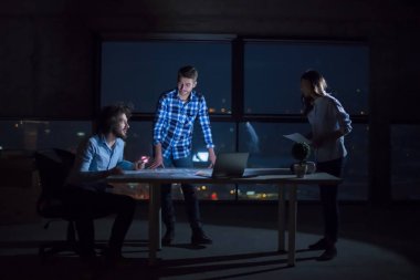 Gruptaki genç iş adamları, inşaat sahasındaki mimar ve mühendis geceleri yeni açılan ofiste dizüstü bilgisayarla belge ve iş akışını kontrol ediyorlar.