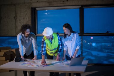Gruptaki genç iş adamları, inşaat sahasındaki mimar ve mühendis yeni açılan ofiste dizüstü bilgisayar kullanarak belge ve iş akışını kontrol ediyorlar.