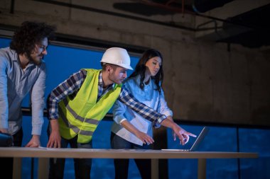 Gruptaki genç iş adamları, inşaat sahasındaki mimar ve mühendis yeni açılan ofiste dizüstü bilgisayar kullanarak belge ve iş akışını kontrol ediyorlar.