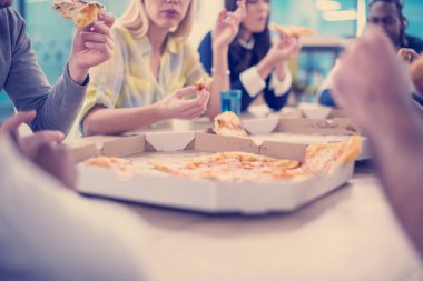 Farklı etnik çeşitlilikte dost canlısı iş adamları başlangıç ofisinde pizzalarını paylaşıyor, çok ırklı iş arkadaşları grubu öğle yemeği arasında eğleniyor ve gülüyor.