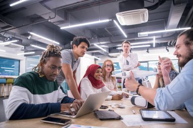 Yeni iş planlarını tartışan, laptop ve tablet bilgisayarlar üzerinde çalışan çok ırklı bir girişim ekibi yeni iş geliştirme teknolojileri hakkında bilgi toplarken,