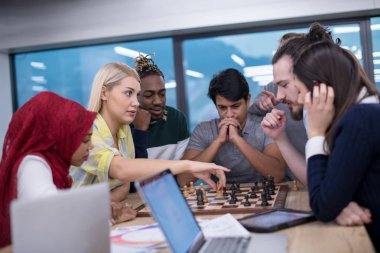 Çok ırklı bir iş adamı grubu modern bir ofis kurarken satranç oynuyor.