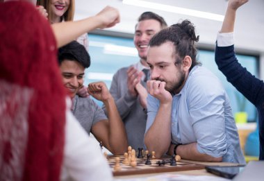 Çok ırklı bir iş adamı grubu modern bir ofis kurarken satranç oynuyor.