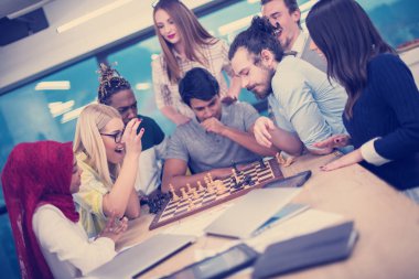 Çok ırklı bir iş adamı grubu modern bir ofis kurarken satranç oynuyor.