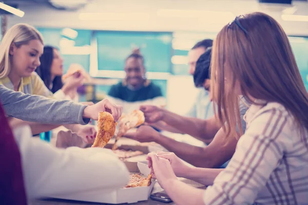 Farklı etnik çeşitlilikte dost canlısı iş adamları başlangıç ofisinde pizzalarını paylaşıyor, çok ırklı iş arkadaşları grubu öğle yemeği arasında eğleniyor ve gülüyor.