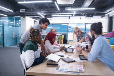 Yeni iş planlarını tartışan, laptop ve tablet bilgisayarlar üzerinde çalışan çok ırklı bir girişim ekibi yeni iş geliştirme teknolojileri hakkında bilgi toplarken,