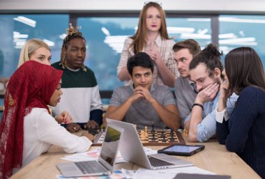 Çok ırklı bir iş adamı grubu modern bir ofis kurarken satranç oynuyor.