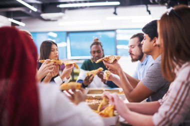 Farklı etnik çeşitlilikte dost canlısı iş adamları başlangıç ofisinde pizzalarını paylaşıyor, çok ırklı iş arkadaşları grubu öğle yemeği arasında eğleniyor ve gülüyor.
