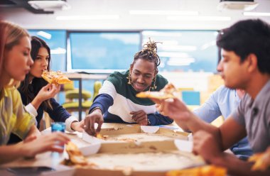 Farklı etnik çeşitlilikte dost canlısı iş adamları başlangıç ofisinde pizzalarını paylaşıyor, çok ırklı iş arkadaşları grubu öğle yemeği arasında eğleniyor ve gülüyor.
