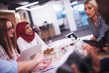 Yeni iş planlarını tartışan, laptop ve tablet bilgisayarlar üzerinde çalışan çok ırklı bir girişim ekibi yeni iş geliştirme teknolojileri hakkında bilgi toplarken,
