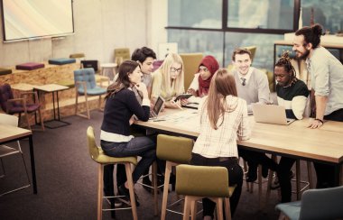 Modern parlak ofis içi beyin fırtınasında toplanan çok ırklı girişim ekibi dizüstü bilgisayar ve tablet bilgisayar üzerinde çalışıyor