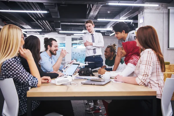 Yeni iş planlarını tartışan, laptop ve tablet bilgisayarlar üzerinde çalışan çok ırklı bir girişim ekibi yeni iş geliştirme teknolojileri hakkında bilgi toplarken,